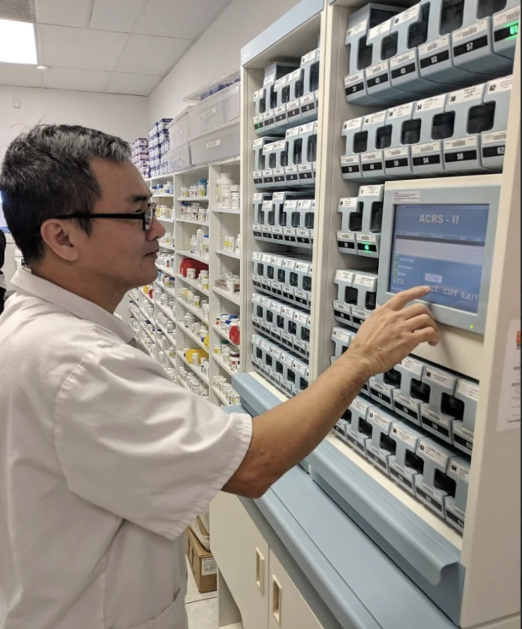 A HealthCo pharmacist using the automated multi-dose packaging machine, surrounded by labelled medication canisters